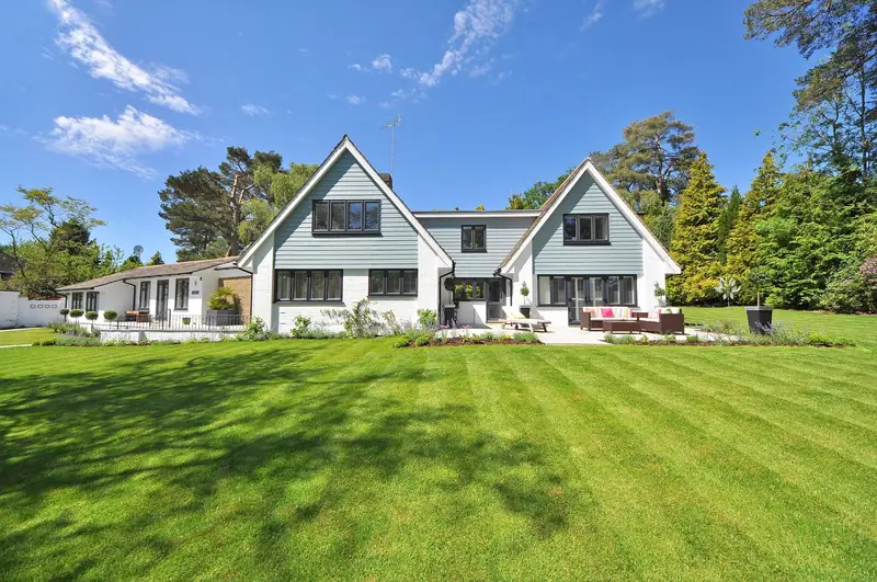 Modern two-storey house with a large rear garden and patio under a clear blue sky