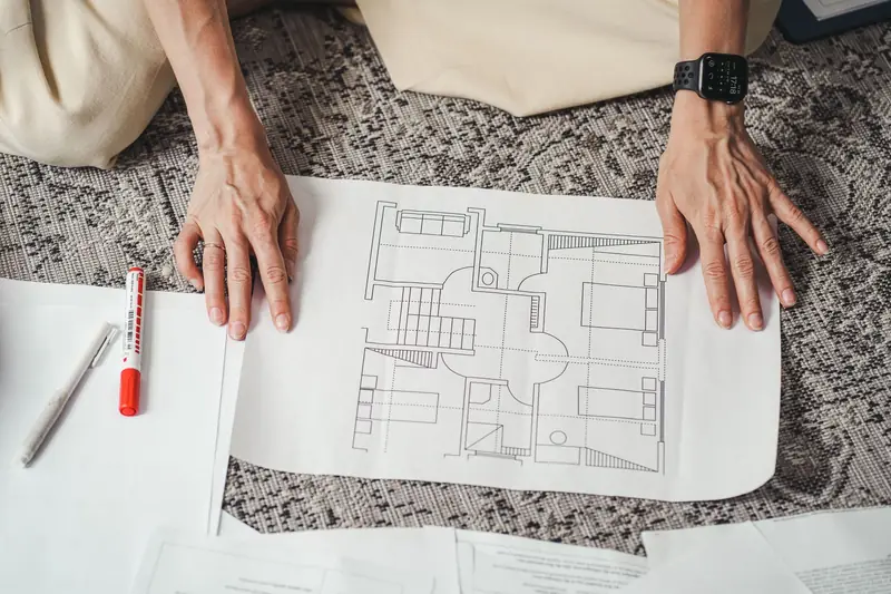 Hands holding a printed house floor plan on a table