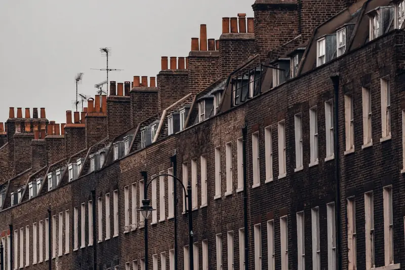 A row of Georgian brick terraced houses in London with mansard roofs, dormer windows and tall chimney stacks against a grey sky